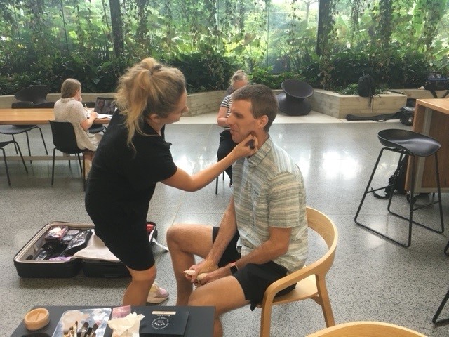 woman putting make up on a man before a photoshoot