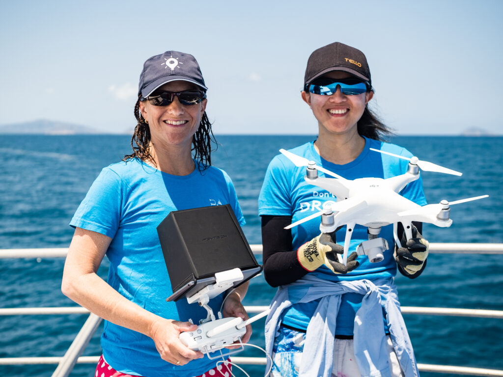 Two people on a boat holding a drone with the ocean in the background