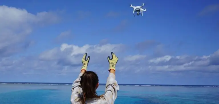 Person waving at a flying drone over water.
