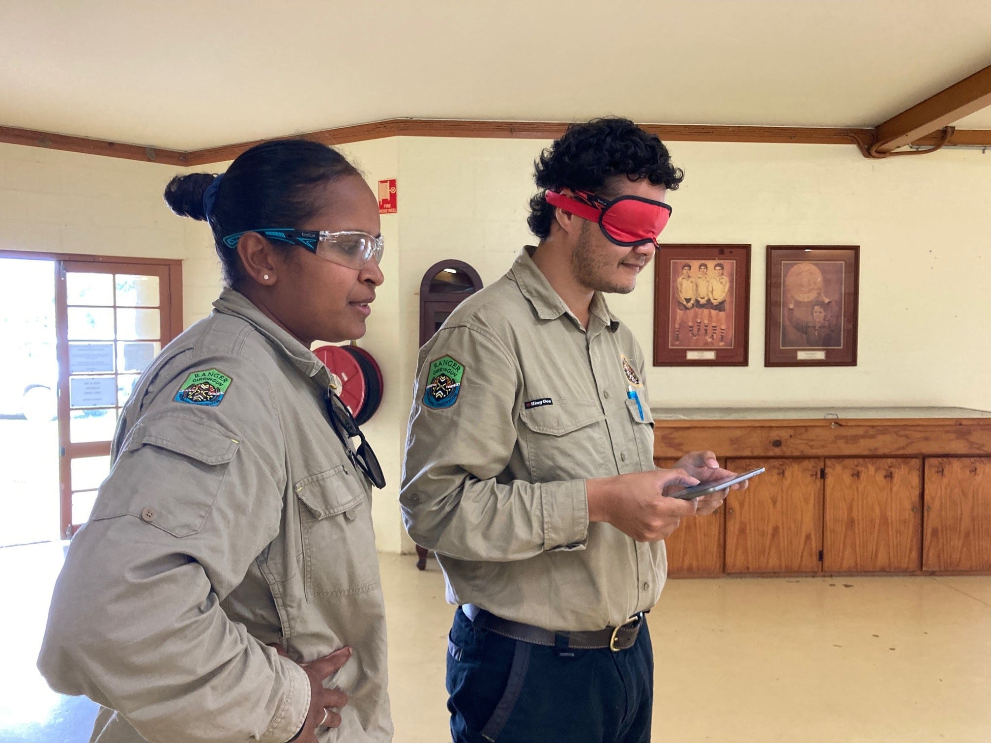 two people flying a drone indoors with blindfolds on