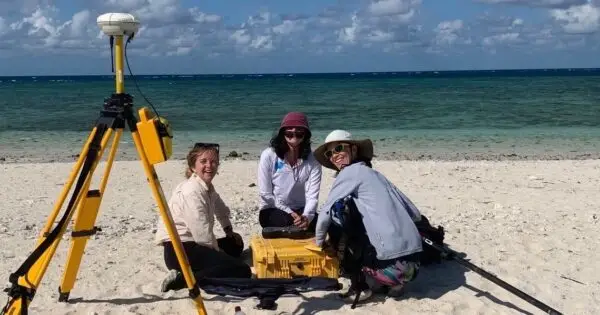 Three people working on a beach with equipment.
