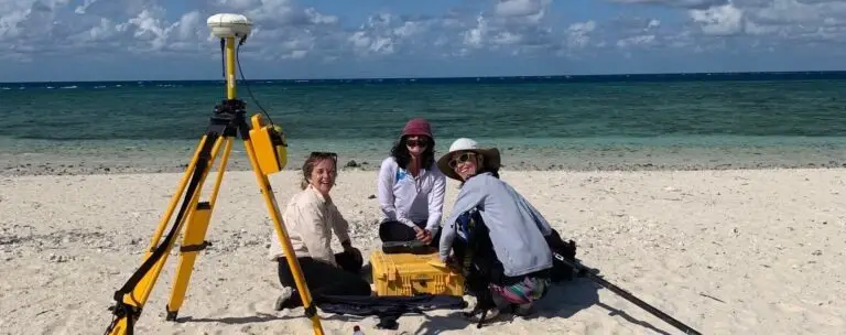 Three people working on a beach with equipment.